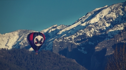 Fortified mountains brace for the passing of a red and white hot air balloon.